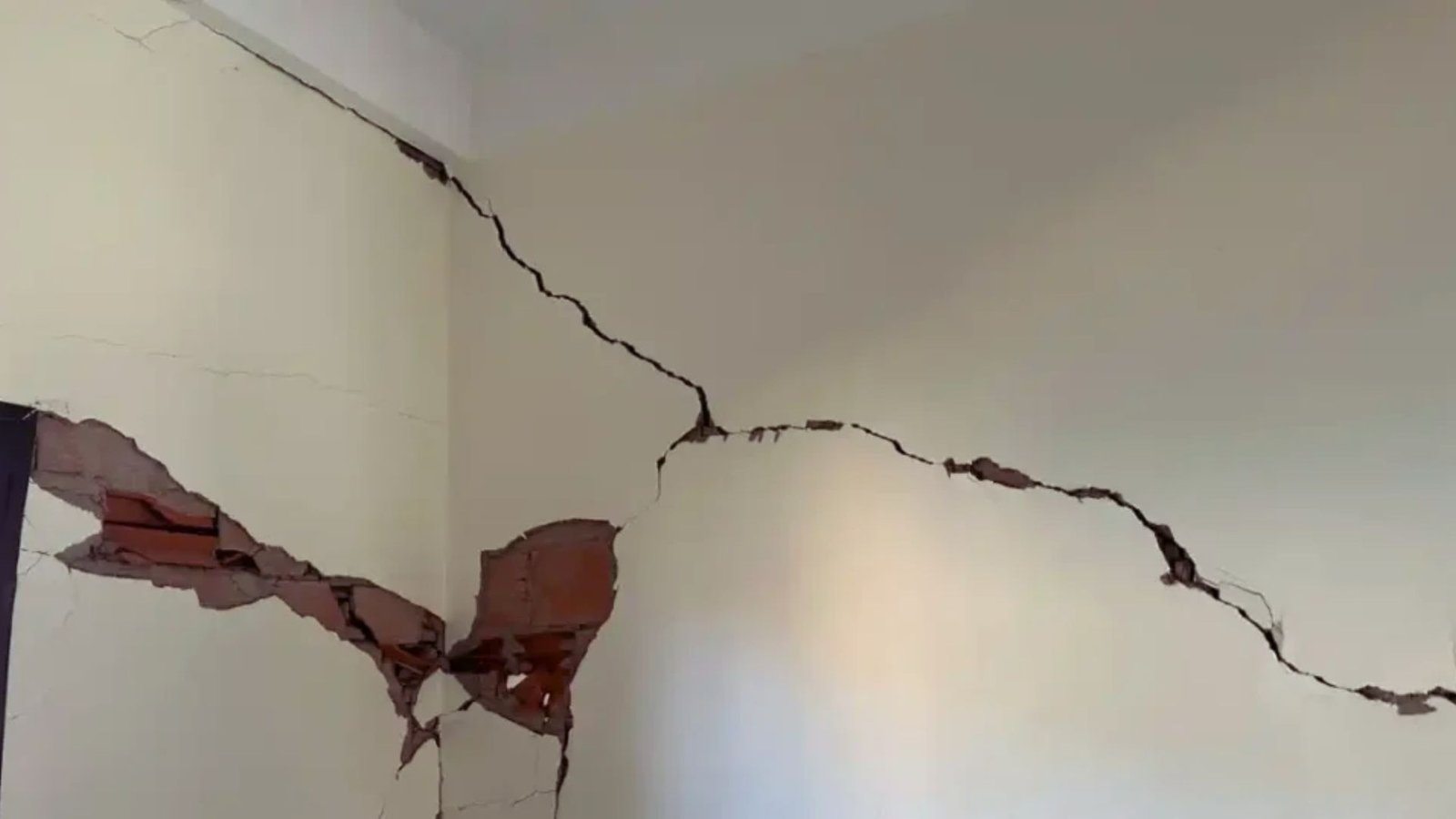 A close-up of a wall showing a crack with a hole, revealing the interior structure behind it.